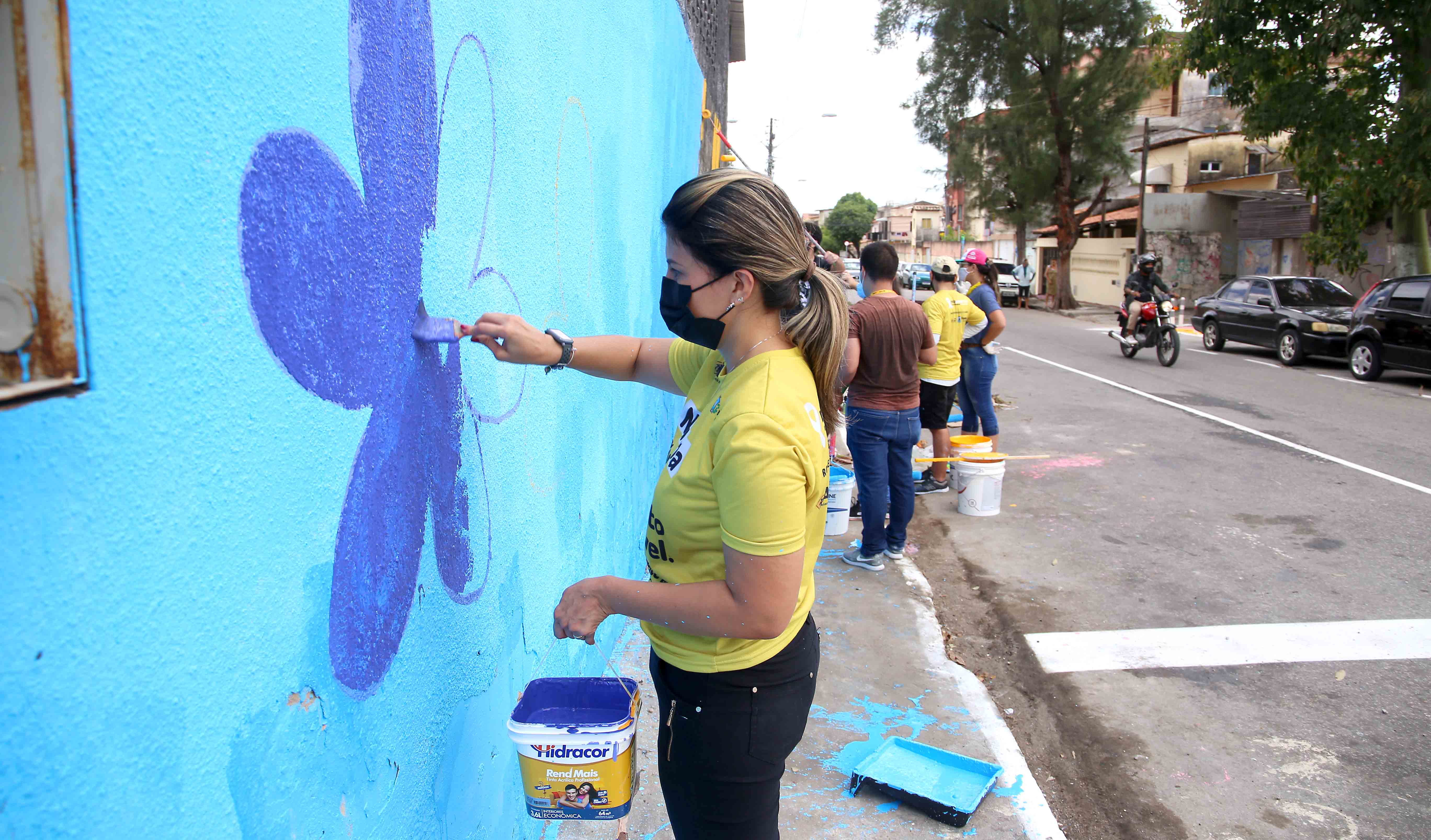 uma mulher pinta uma flor vermelha em um muro na rua